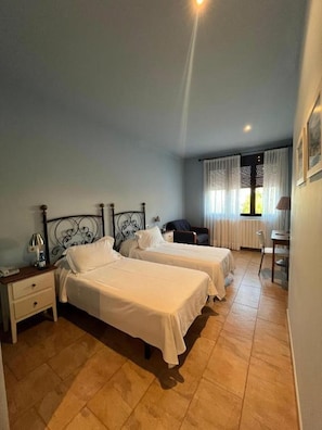 A hotel room with two beds, a desk, a chair, and a window with curtains. - HOTEL NOVELLA (Benassal)