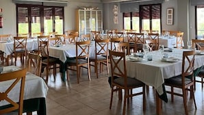 Zona pranzo con diversi tavoli e sedie, ampie finestre e pavimento piastrellato.
