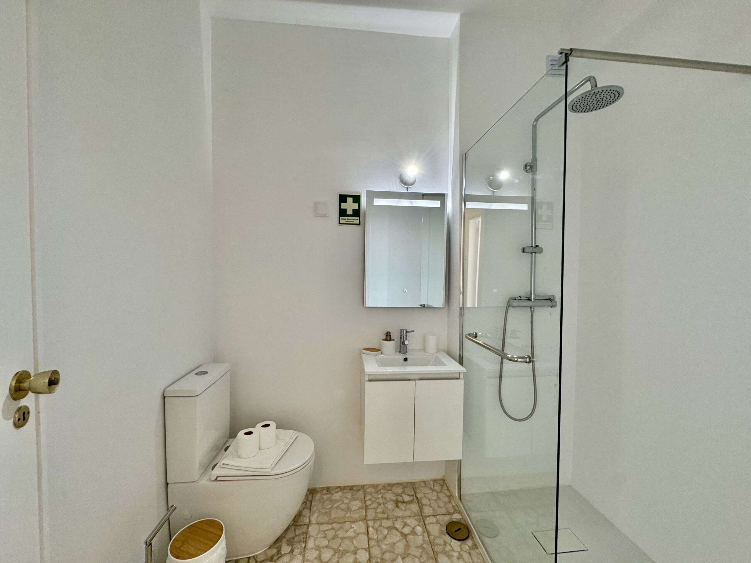 A modern bathroom with a glass-enclosed shower, a sink with a mirror above, a toilet, and a trash bin.