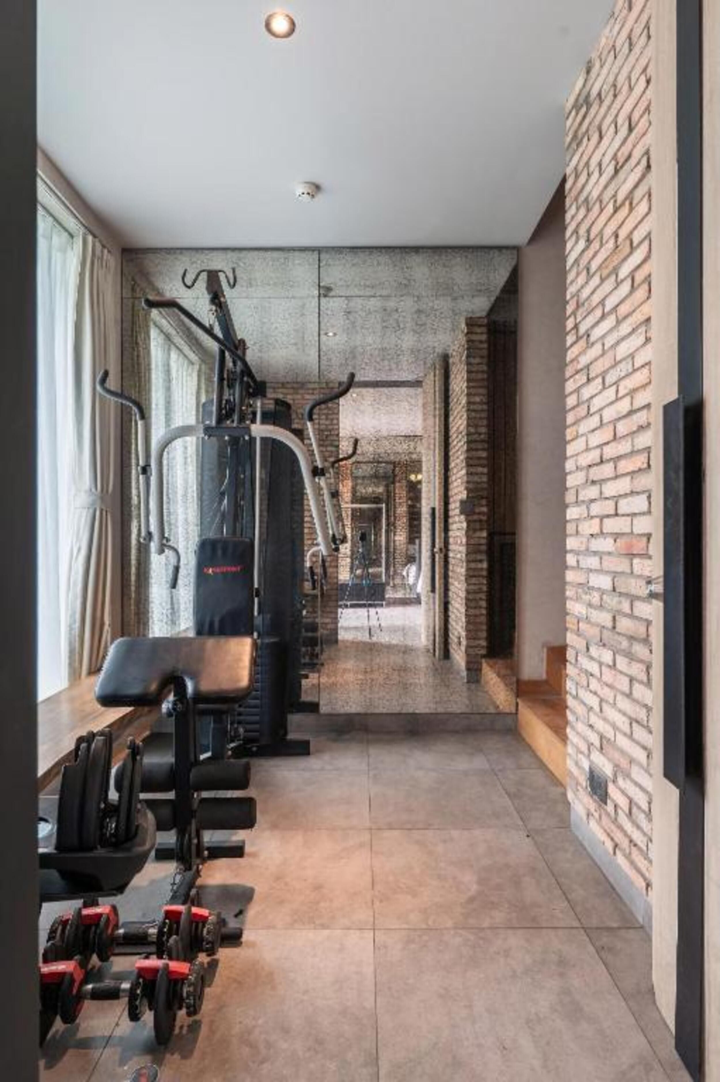 A gym with exercise equipment, a brick wall, and a window.