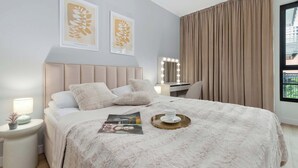 A bedroom with a bed, bedside table, lamp, and a window with curtains. - Beige and Blue Apartment | Garden | Parking (Gdańsk)