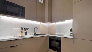 A compact kitchen with a microwave, oven, sink, and modern cabinetry. - Beige and Blue Apartment | Garden | Parking (Gdańsk)