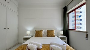 Ett hotellrum med en säng, två sängbord, ett fönster med utsikt över byggnader och en mönstrad matta.