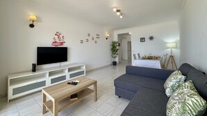 Ett modernt vardagsrum med en platt-TV, ett soffbord i trä, en grå soffa och en matplats i bakgrunden.