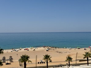 A beach with umbrellas, lounge chairs, and palm trees. - Quarteira Beach & Ocean View 3 by Homing (Loulé)