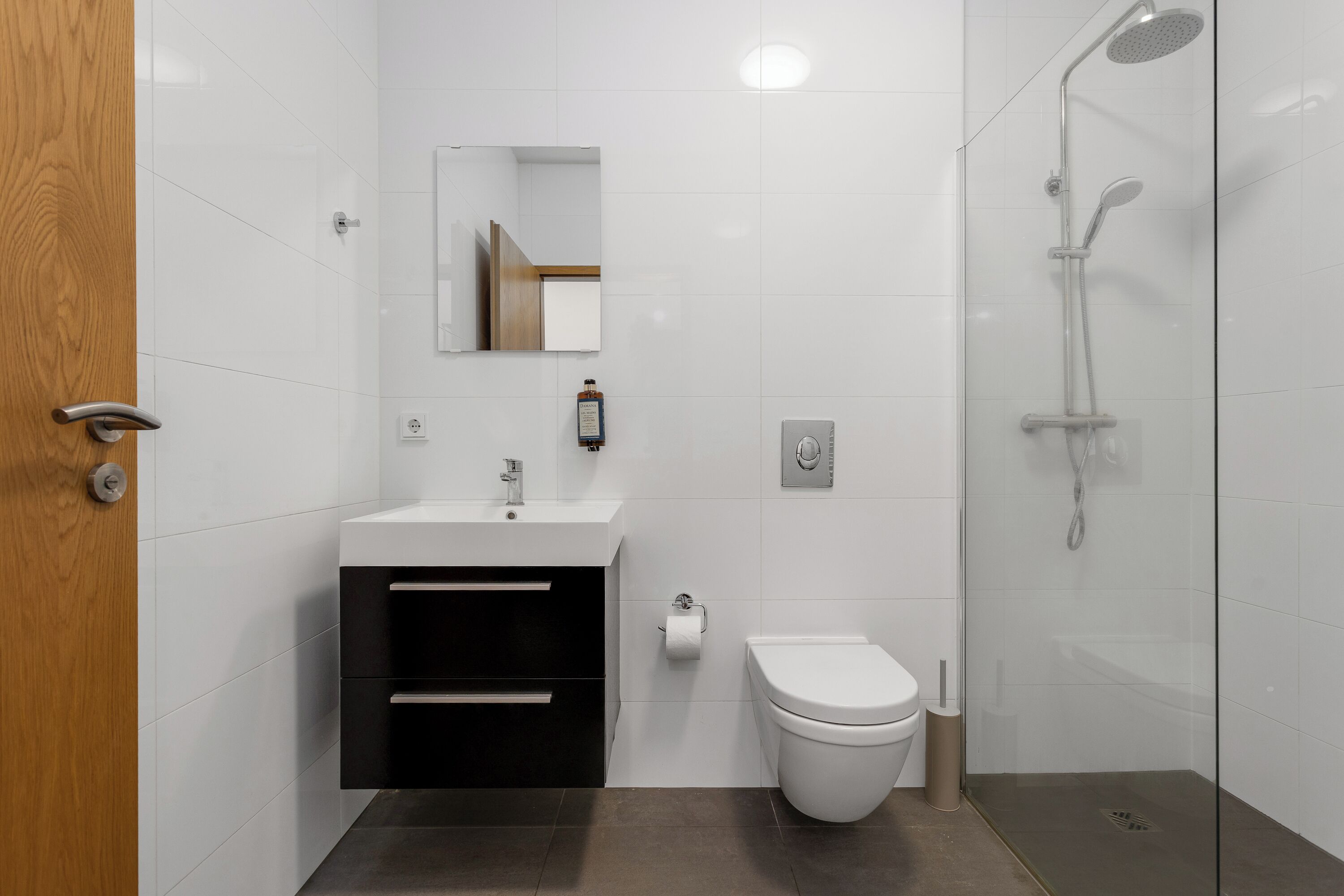 Uma casa de banho moderna com uma pia branca, armário preto, sanita e cabine de duche com vidro.