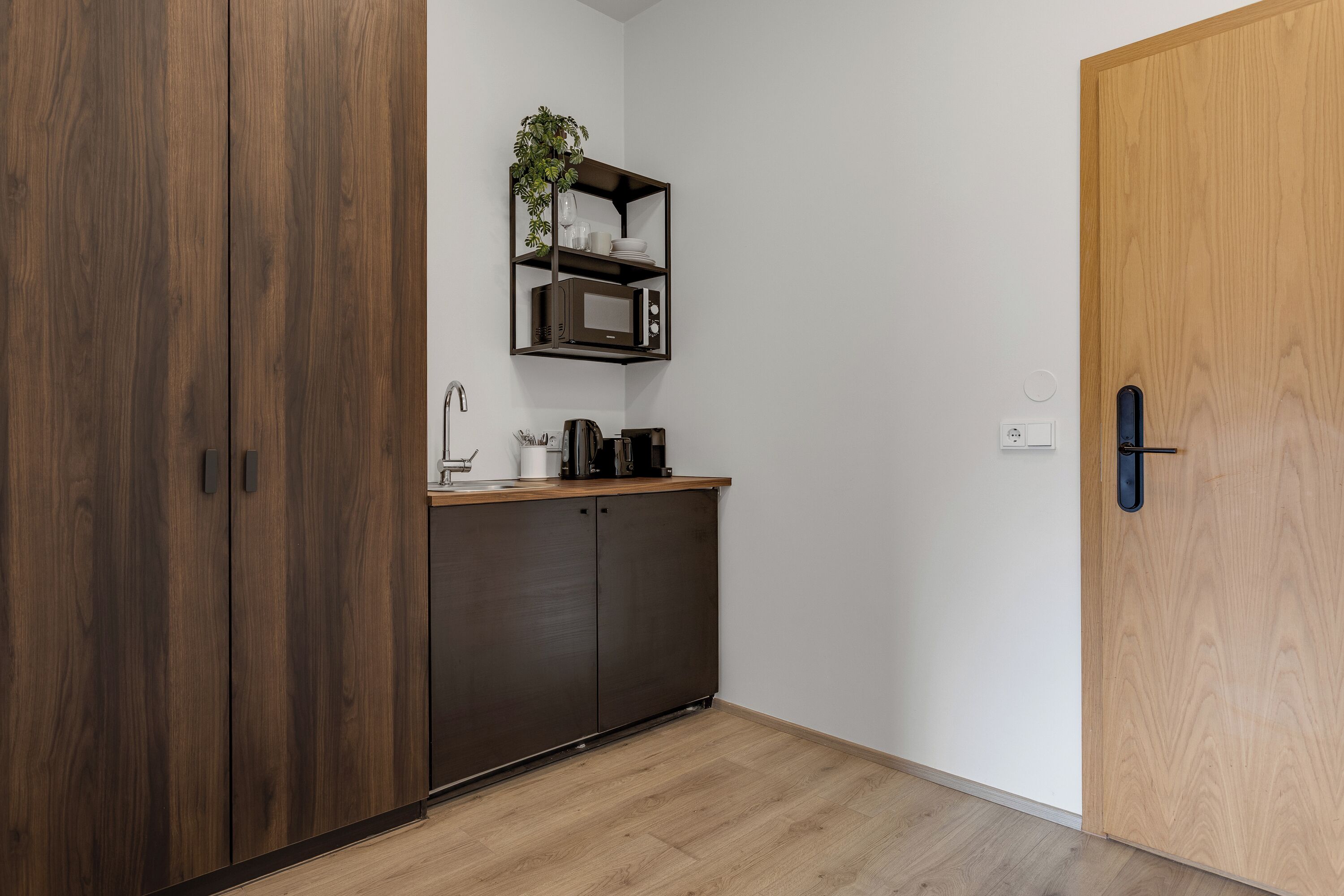 A compact kitchen with dark wooden cabinets, a microwave, and a small shelf with a plant.