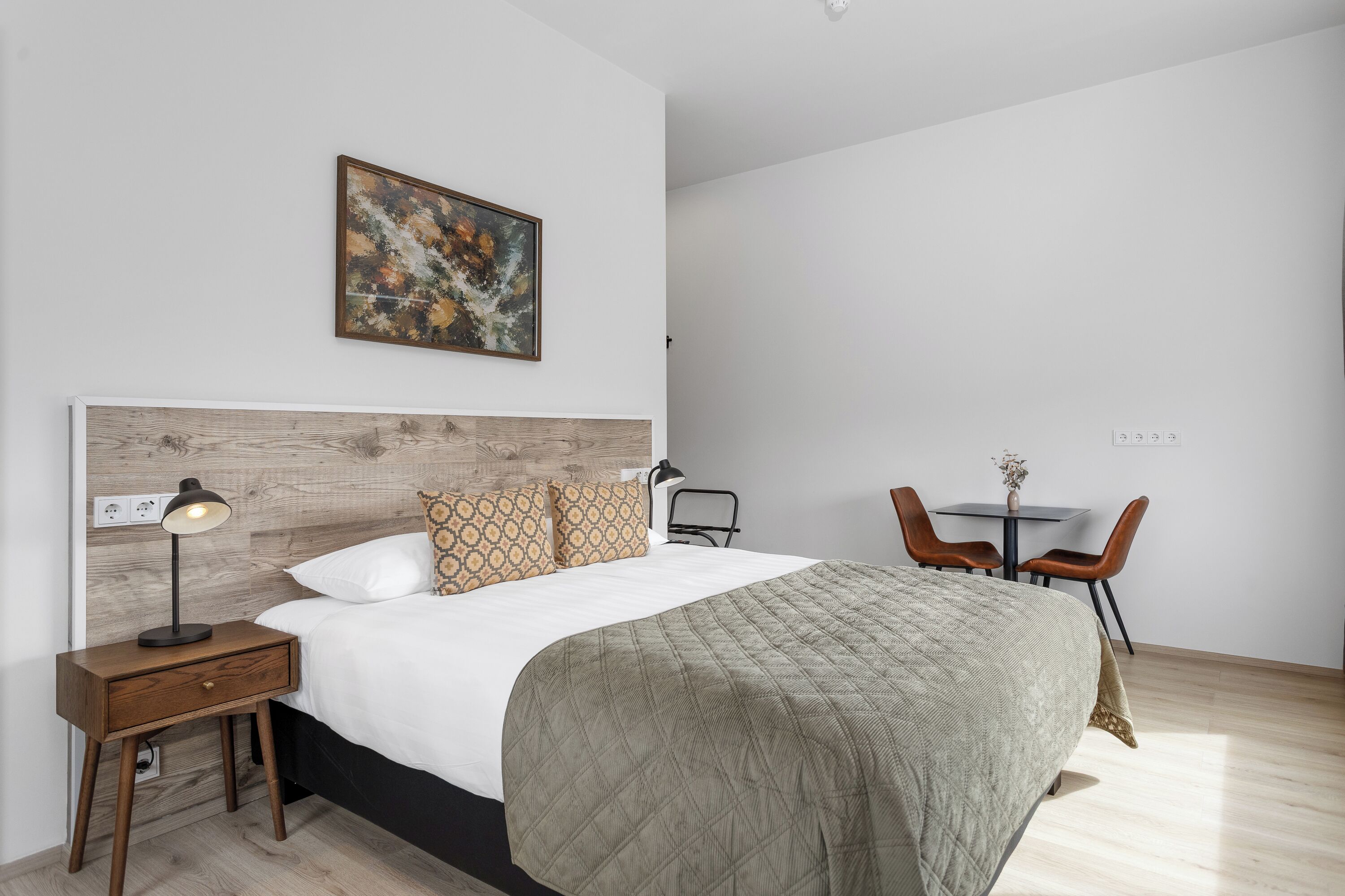 A bedroom with a bed, bedside table, lamp, and a small table with chairs.