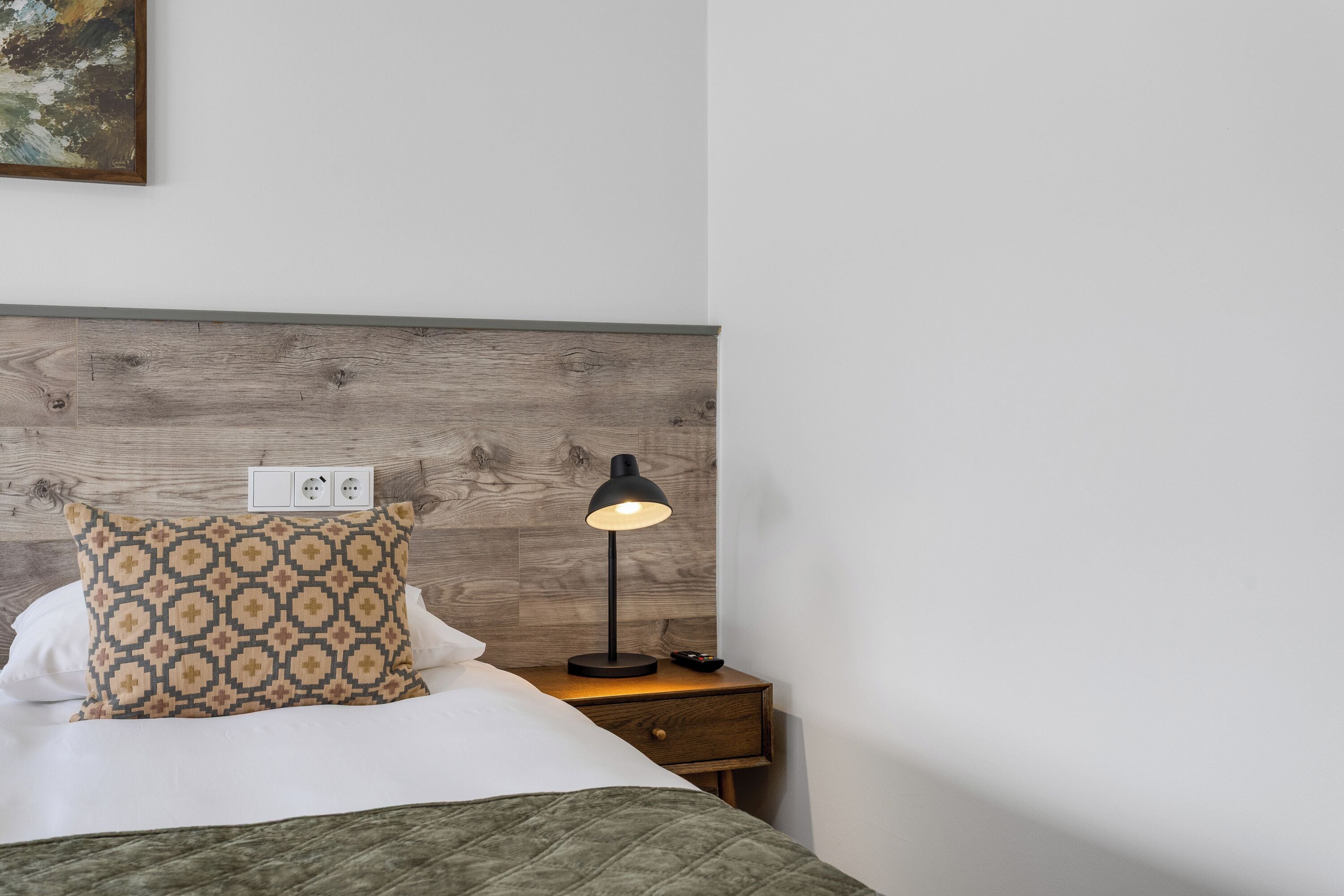 A neatly made bed with a patterned pillow, a bedside lamp, and a wooden headboard.