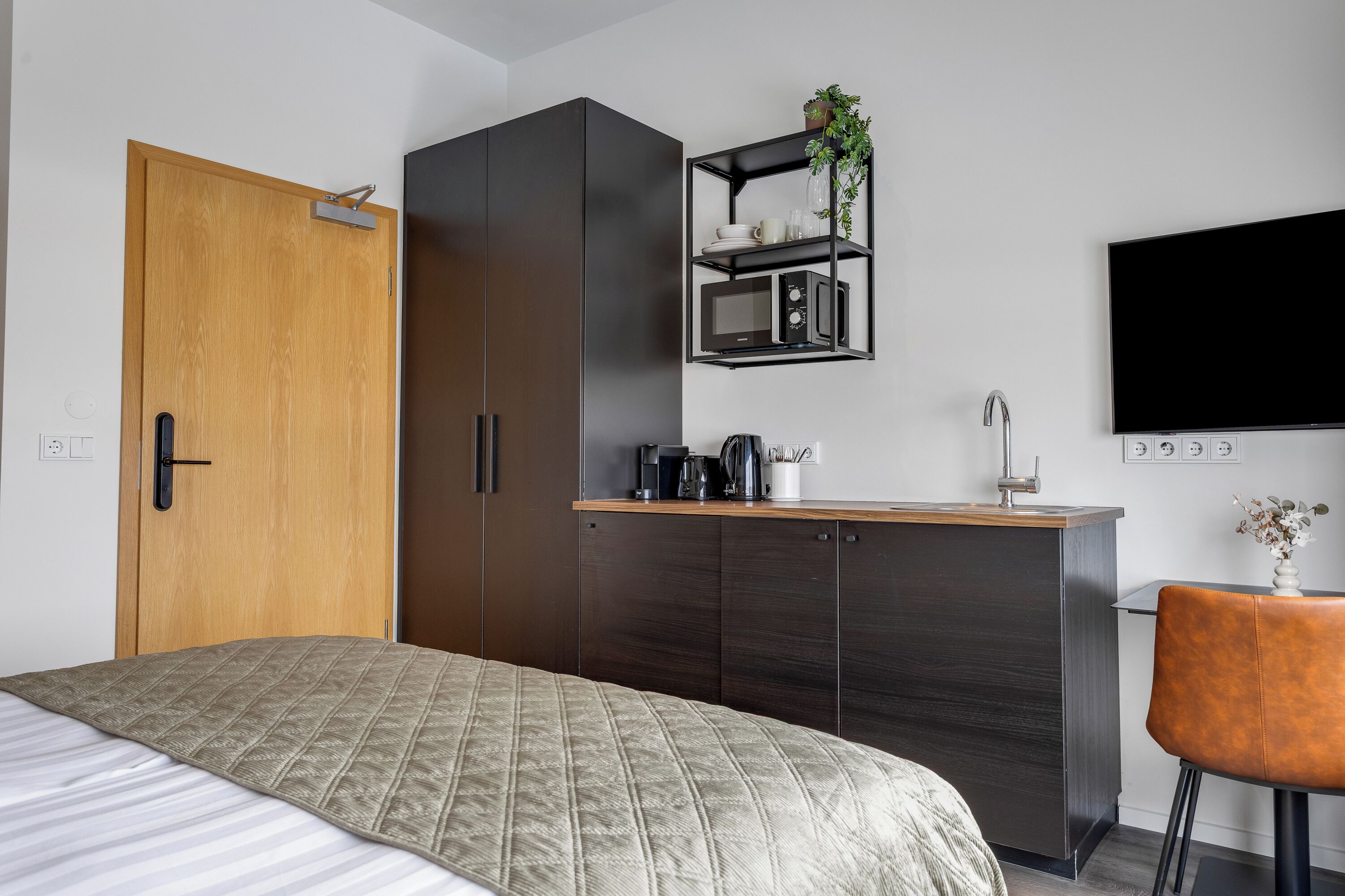 Un dormitorio con cama, armario, kitchenette, televisor y una silla.