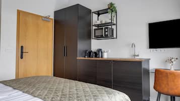 Un dormitorio con cama, armario, kitchenette, televisor y una silla.