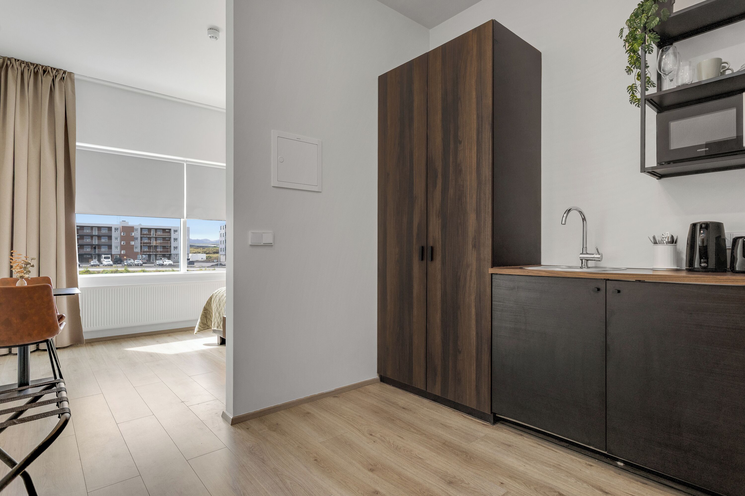 A modern kitchen with a dark wood cabinet, a built-in microwave, and a window with a view of buildings.