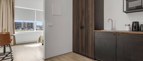 A modern kitchen with a dark wood cabinet, a built-in microwave, and a window with a view of buildings.