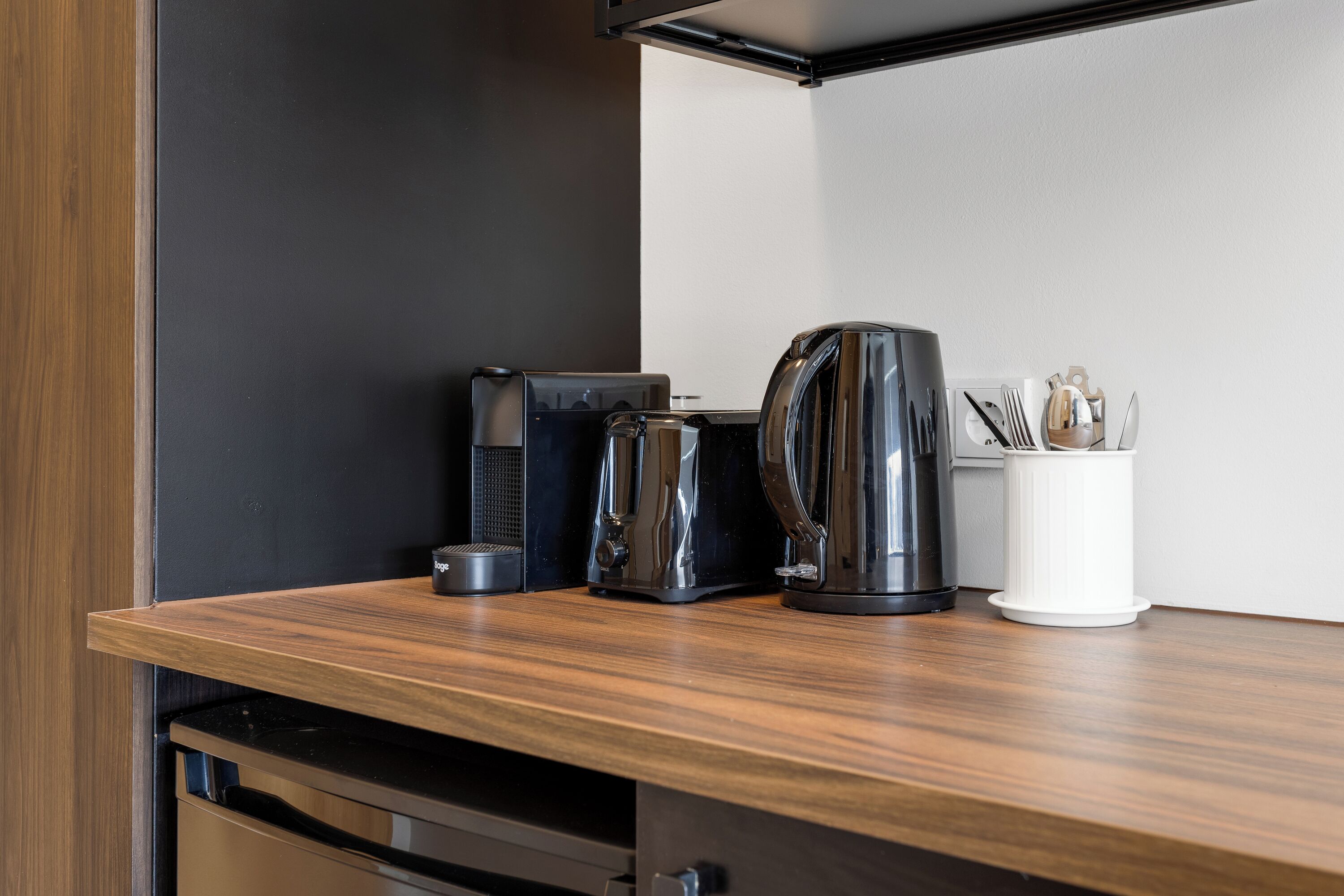 A kitchen counter with a coffee maker, a kettle, and a utensil holder.