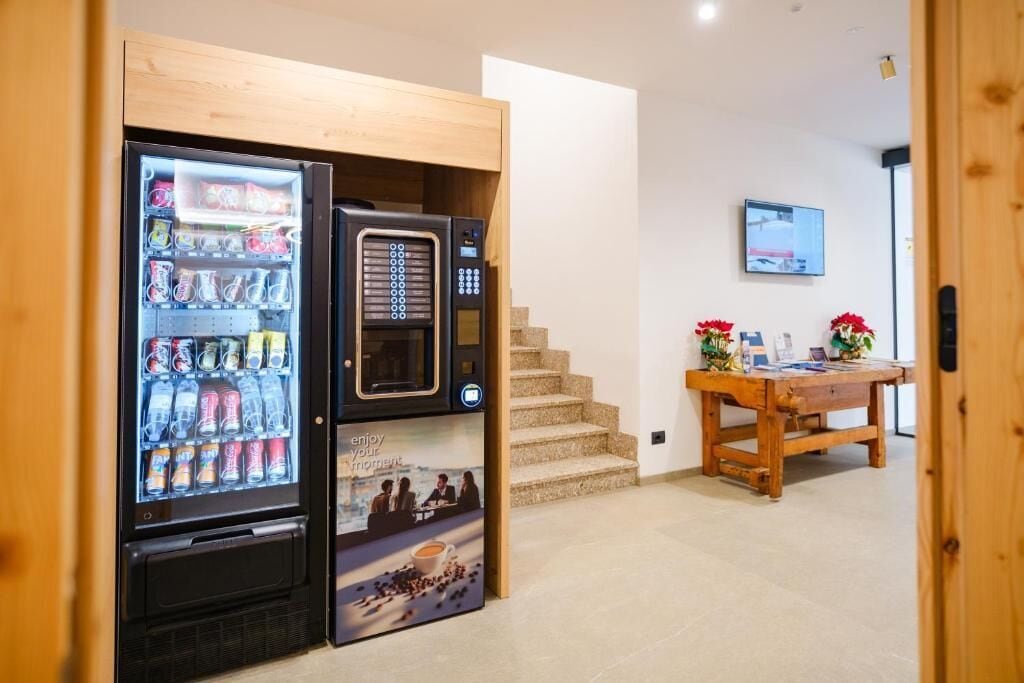 A vending machine with beverages and snacks, a microwave, and a table with flowers and a laptop.