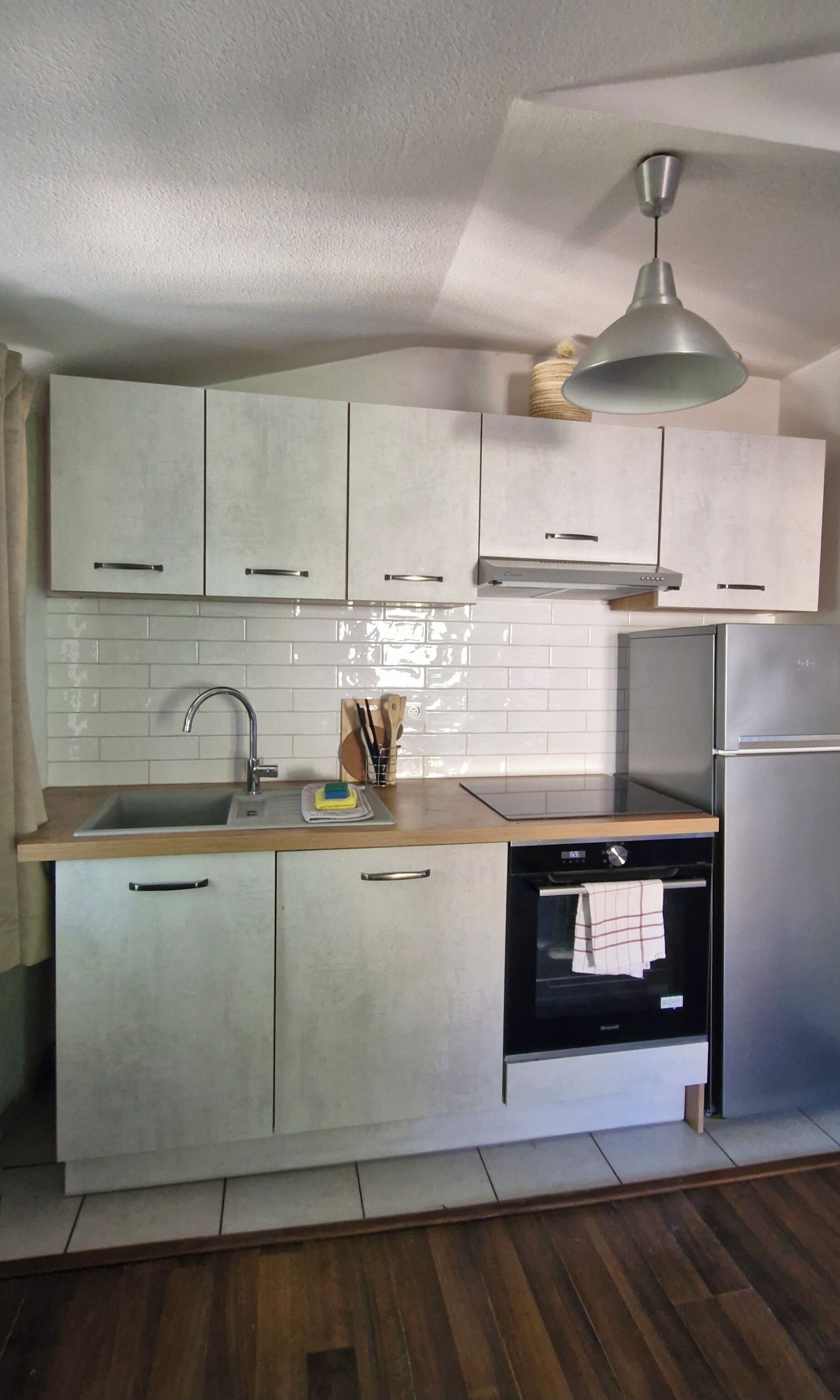 A kitchen with white cabinets, a stainless steel refrigerator, a built-in oven, and a hanging light fixture.