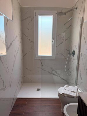 Une salle de bain moderne avec une douche à parois de verre, des toilettes et une fenêtre.