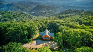 Une maison entourée d’une forêt dense, avec une chaîne de montagnes en arrière-plan.