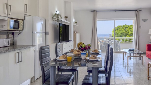 Uma cozinha moderna com eletrodomésticos embutidos, um espaço de refeições com mesa posta para dois e uma varanda com vista.