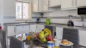 Uma cozinha moderna com armários brancos, uma mesa de jantar com itens de café da manhã e uma janela com cortinas.