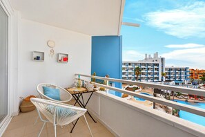 Ein Balkon mit Korbstühlen, einem kleinen Tisch und Blick auf ein Schwimmbecken sowie Gebäude.