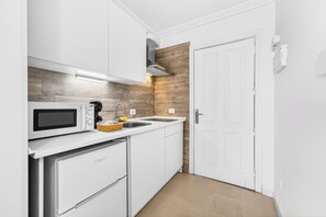 Eine kleine Küche mit weißen Schränken, einer Mikrowelle, einem Spülbecken und einem eingebauten Backofen.