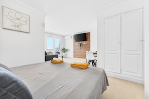 A hotel room with a bed, a TV mounted on a wooden panel, a white wardrobe, and a framed artwork on the wall. - Home Holidays 444 (CN)
