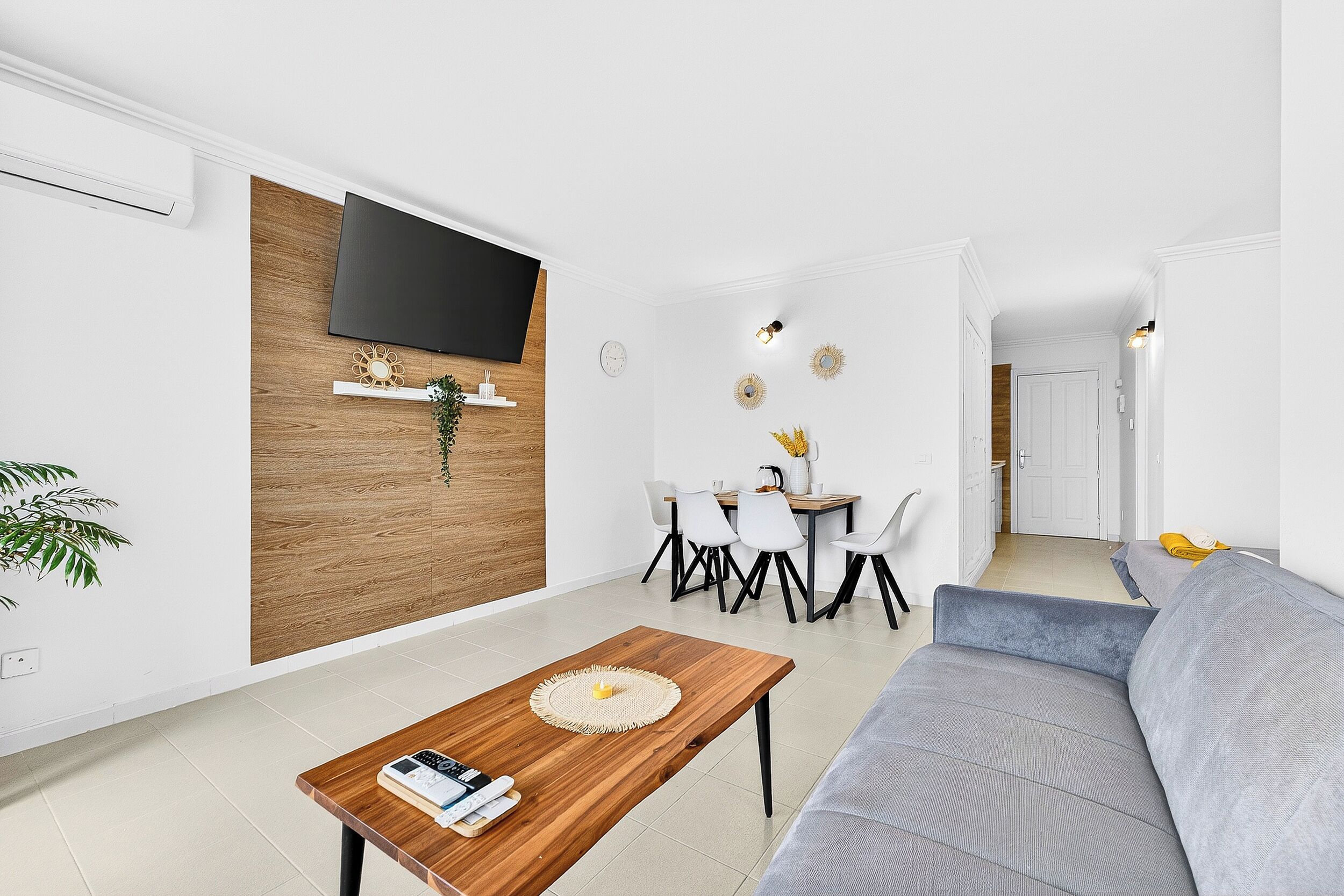 Un salon moderne doté d’un téléviseur à écran plat, d’un mur décoratif en bois, d’un coin repas avec des chaises et d’un canapé.
