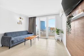 A modern living room with a sofa, a coffee table, a TV mounted on the wall, and a sliding glass door leading to an outdoor balcony. - Home Holidays 444 (CN)