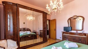 Un dormitorio con un armario grande, una cama con ropa de cama verde, un televisor en una cómoda y una araña.