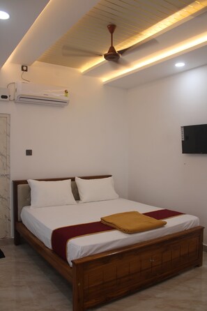 Une chambre à coucher avec un lit en bois, du linge de lit blanc, un plaid rouge, un ventilateur de plafond, un climatiseur et un téléviseur fixé au mur.