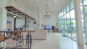A spacious living area with a high ceiling, a dining area with bar stools, a sofa, and a television.