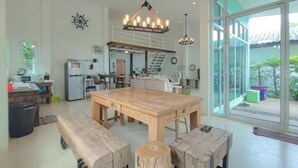 A spacious kitchen with a large wooden table and benches, a dining area, and a view through large windows.