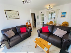 A living room with two dark leather sofas, a wooden coffee table, and a dining area with a wicker chair and a table.