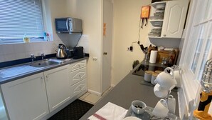 A compact kitchen with white cabinets, a built-in microwave, and a small window with blinds.