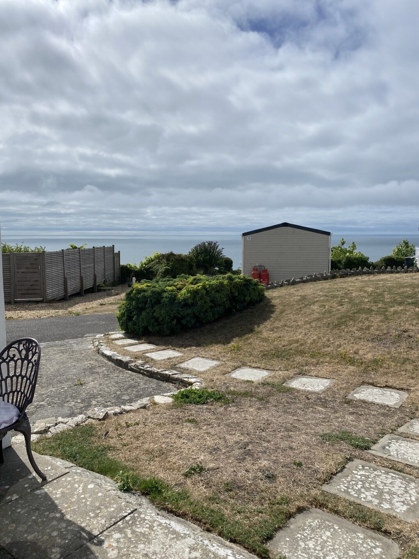 A grassy yard with a paved path, a small shed, and a chair.