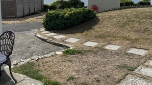 A grassy yard with a paved path, a small shed, and a chair.