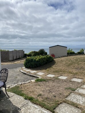 Une cour gazonnée avec un chemin pavé, un petit abri de jardin et une chaise.