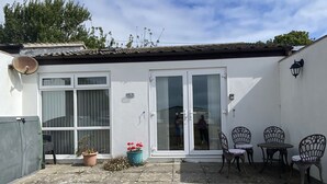 A white building with a tiled roof, a glass door, and a small patio with chairs and potted plants.