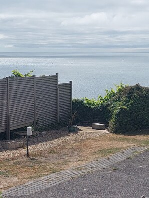 Vista de uma área costeira com uma cerca de madeira, uma planta em vaso e um caminho pavimentado que leva até a água.