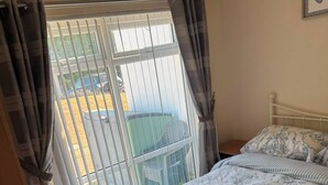 A bedroom with a bed, curtains, a window with blinds, a bedside table, and a wall-mounted light fixture.