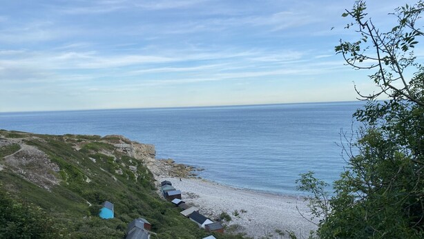 A coastal area with a row of small, simple houses with sloped roofs, situated on a pebbly beach.