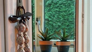 Une porte ornée d’une guirlande de perles décoratives et d’un nœud, une fenêtre donnant sur des plantes en pot à l’extérieur.