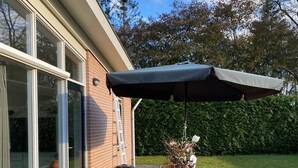 Une terrasse avec une table en bois, des chaises, un barbecue et un parasol.