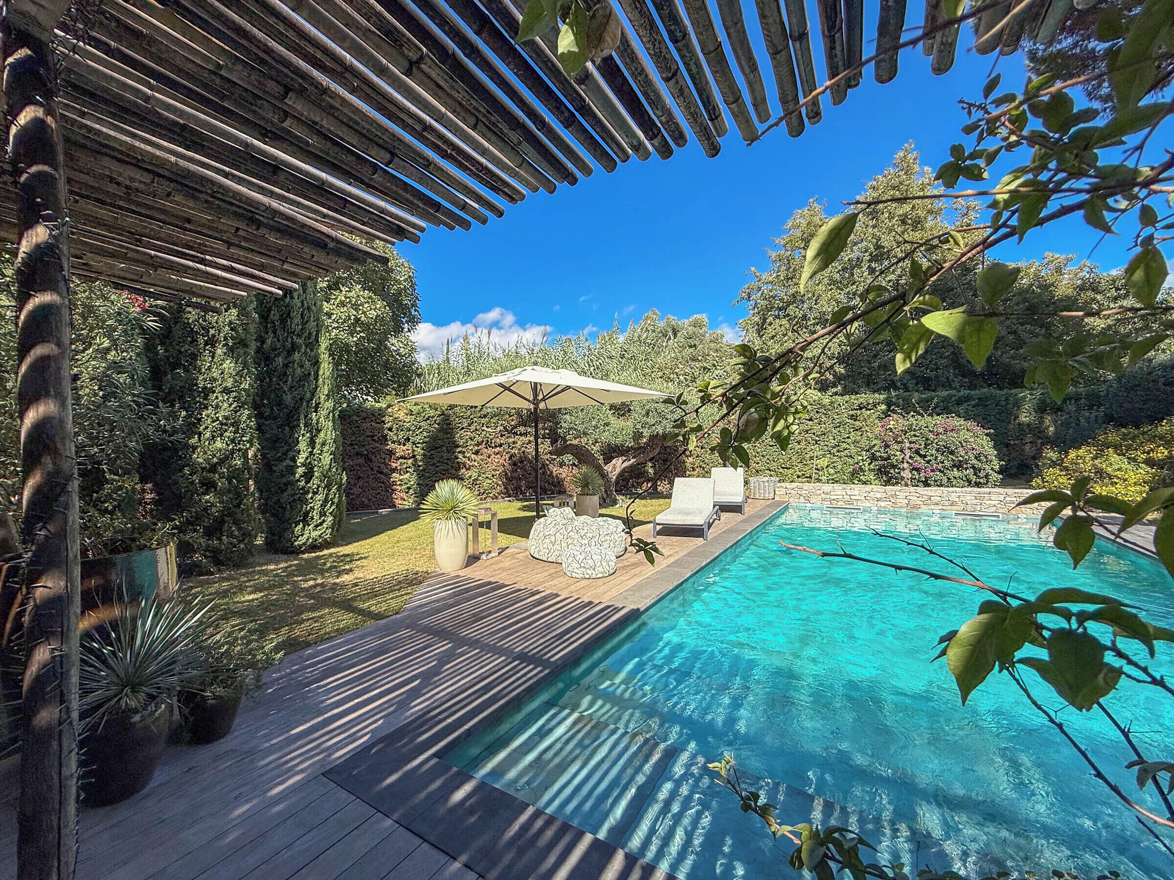 A swimming pool with a wooden deck, lounge chairs, and a pergola.