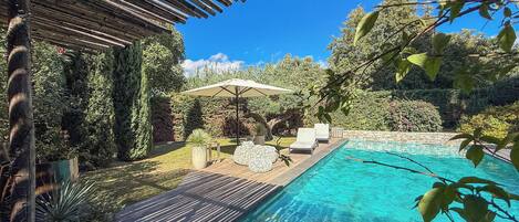 A swimming pool with a wooden deck, lounge chairs, and a pergola.