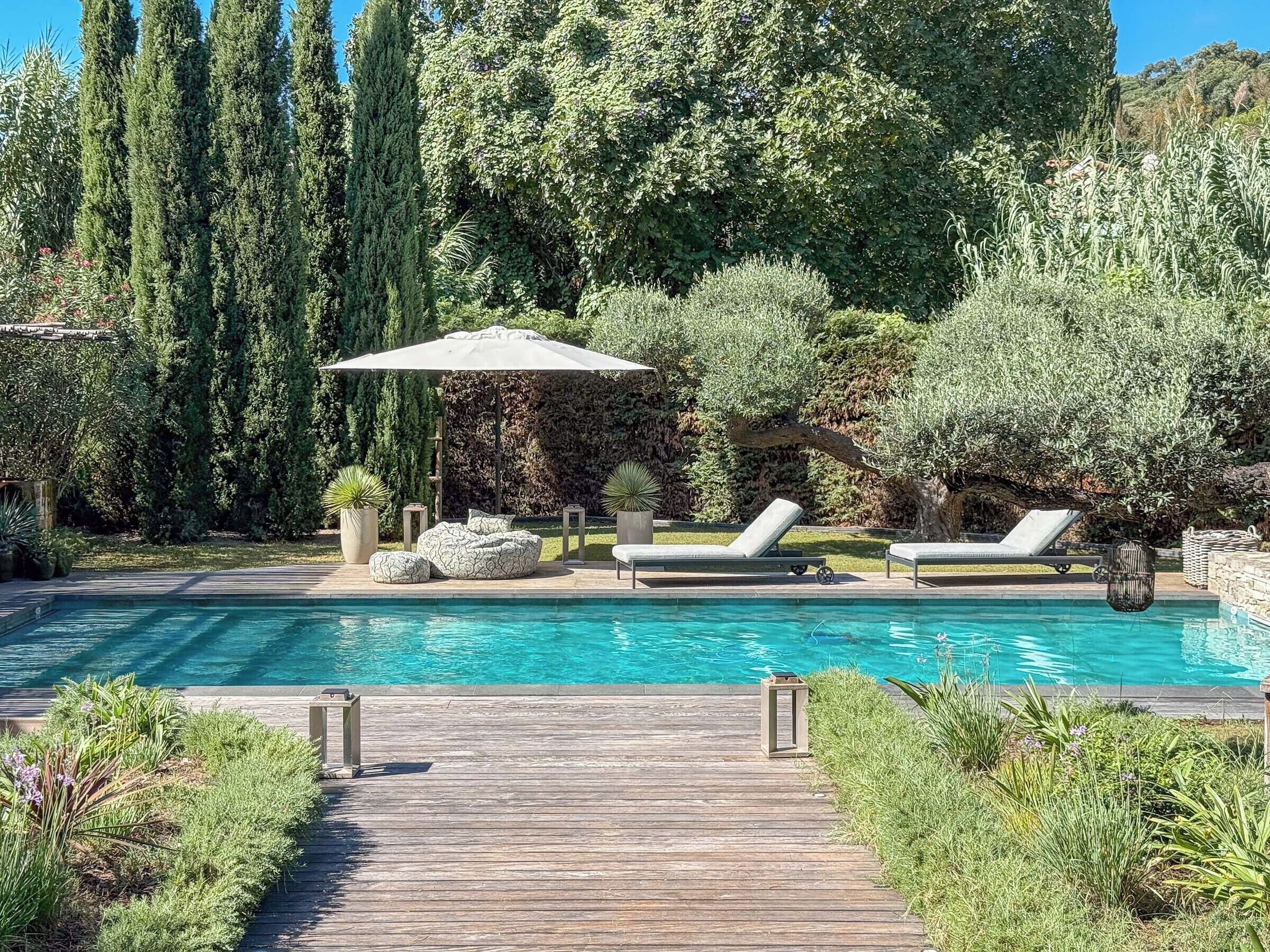 A swimming pool with lounge chairs, a wooden deck, and surrounding greenery.
