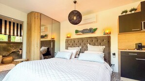 A bedroom with a large bed, a mirror, a hanging light fixture, and a view of the outdoors. - Recently renovated villa with a fantastic garden not far from the beaches of Gigaro (La Croix-Valmer)