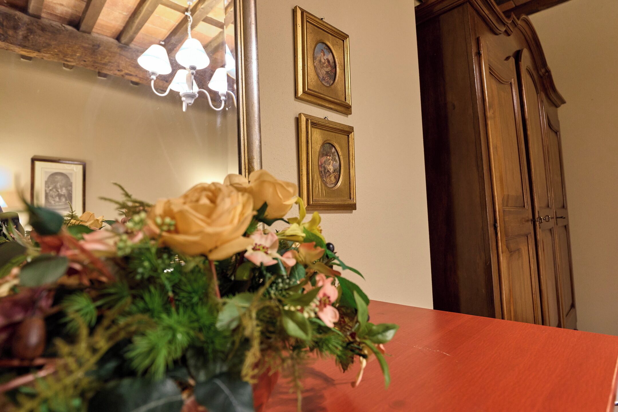 A room with a wooden table, a floral arrangement, a chandelier, and two framed pictures on the wall.