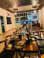 A restaurant with wooden tables and chairs, a long counter, and large windows.
